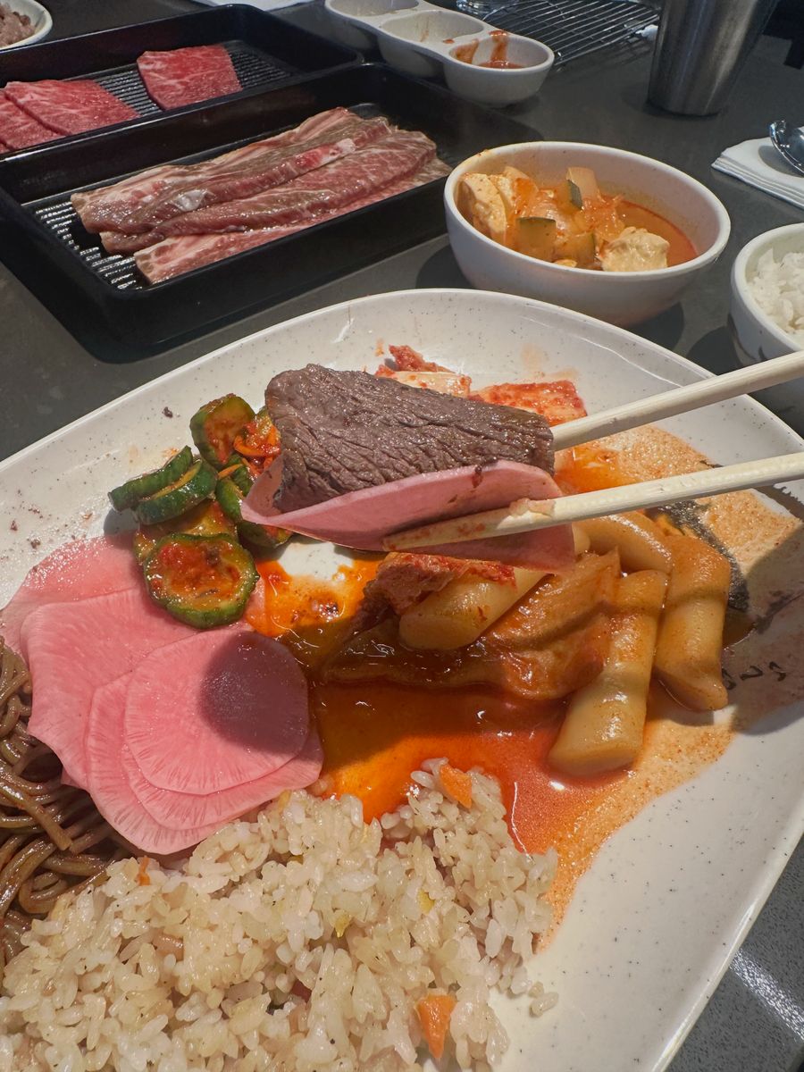 A finished plate with rice and banchan, chopsticks in hand